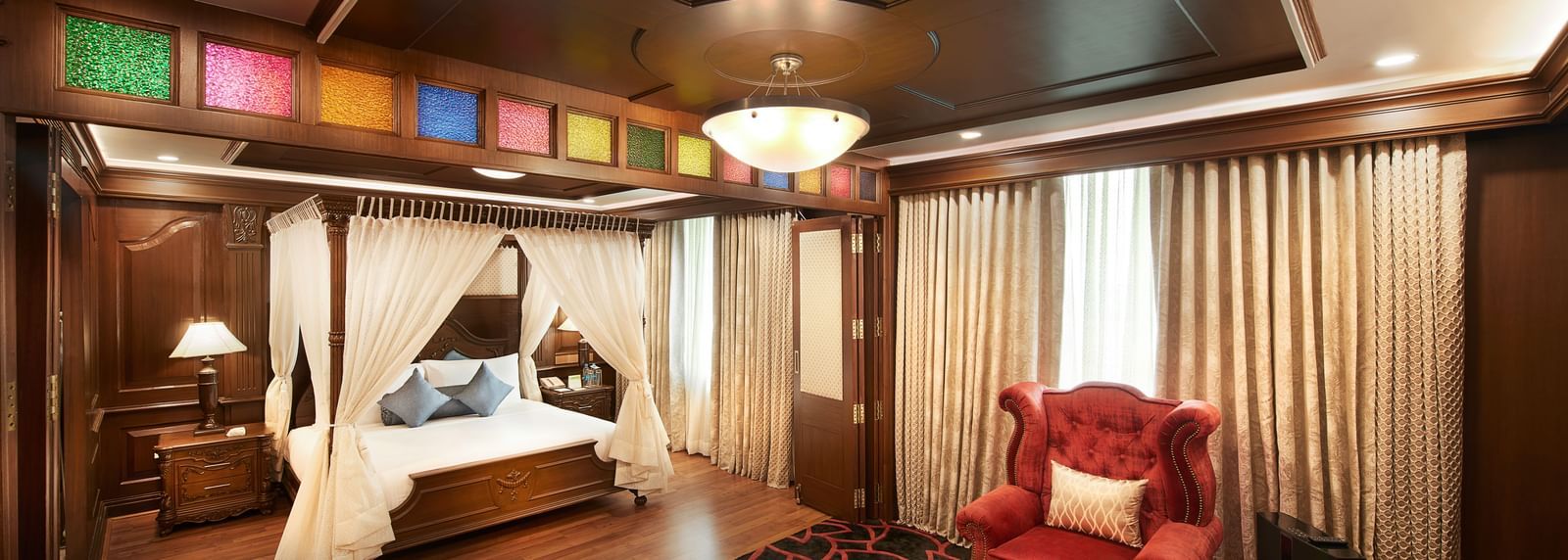An image of a bedroom with poster bed, bedside table with lamp, and a seating area with sofa sets - Accord Hotels and Resorts